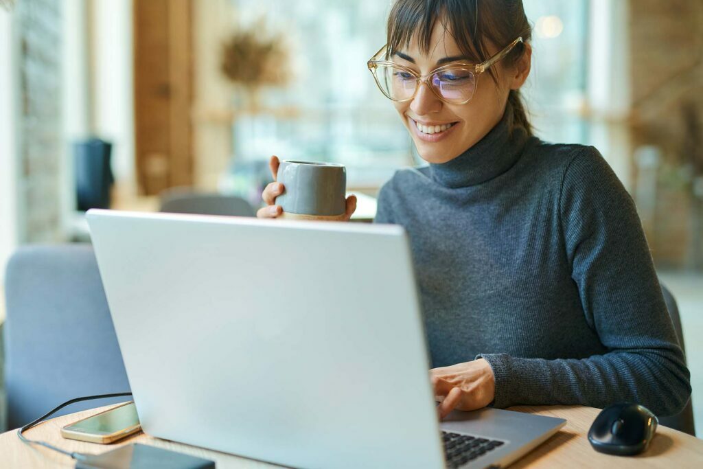 happy lady drinking coffee while on her computer reading business content