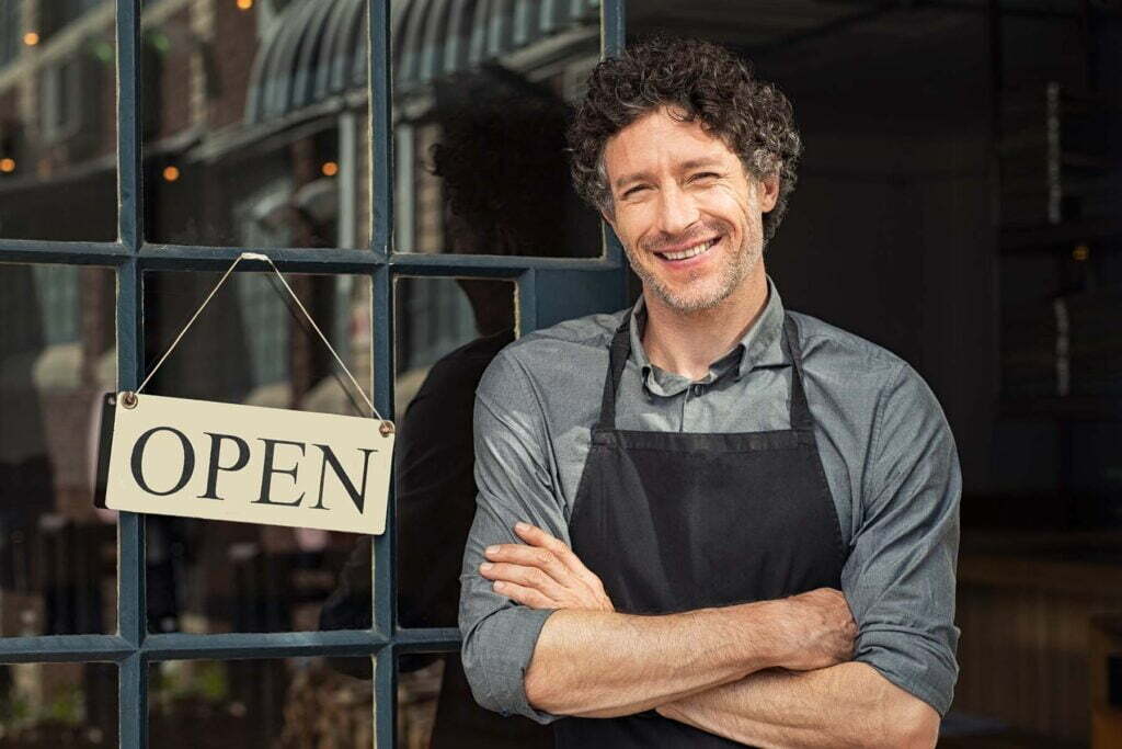happy business man in apron in front of his open store