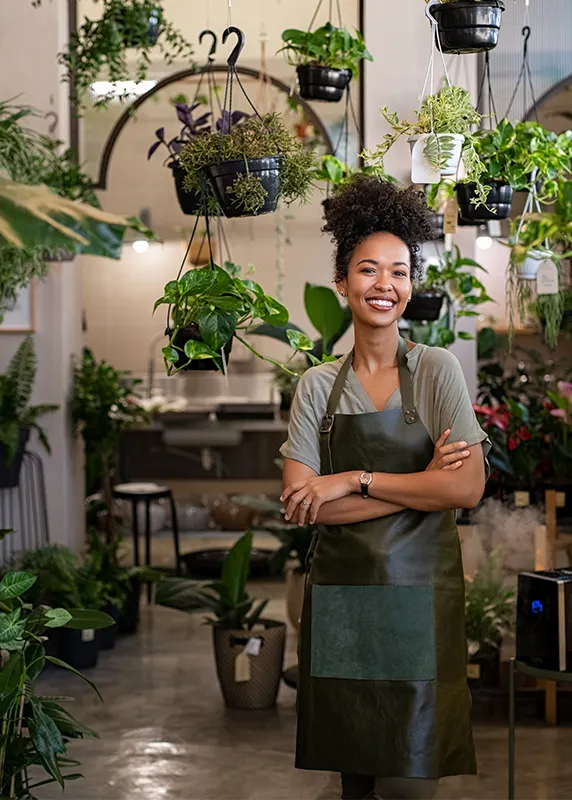 woman plant store owner wearing apron in front of hanging plants
